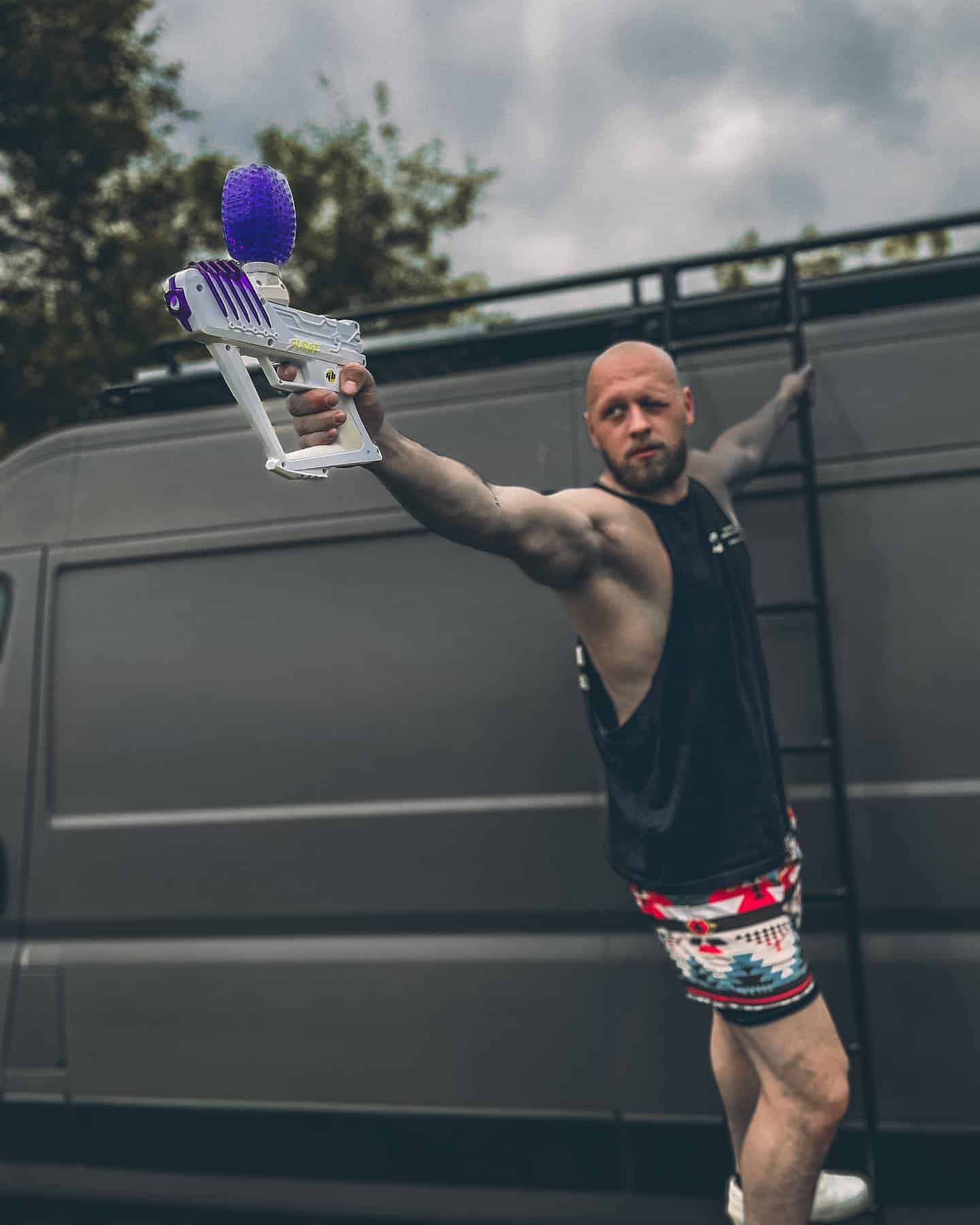man shooting a gel blaster while hanging on a ladder