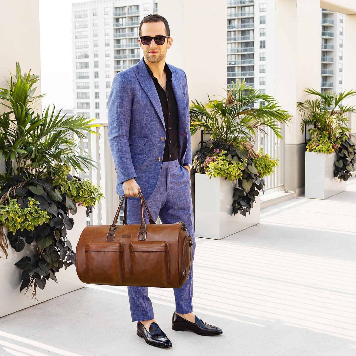 man in a suit carrying a leather garment bag