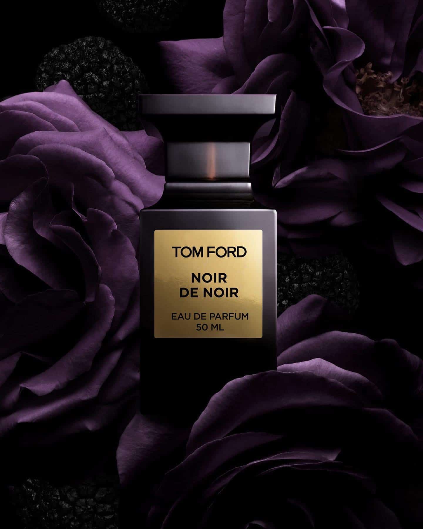 a bottle of tom ford noir de noir surrounded with purple flowers