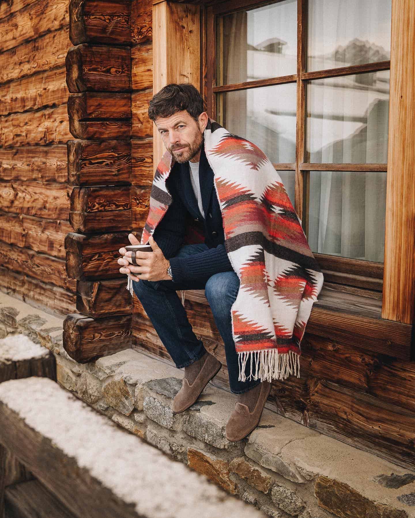 man holding a cup sitting on a windowsill