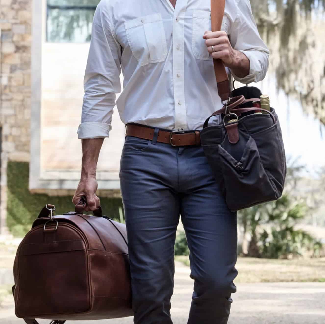 Man holding a leather duffle bag and a shoulder bag with bottles in it