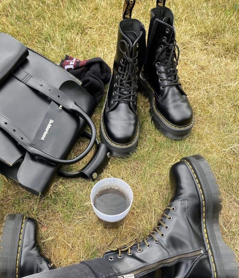 person sitting on the ground with pairs of doc martens and a dr martens bag 