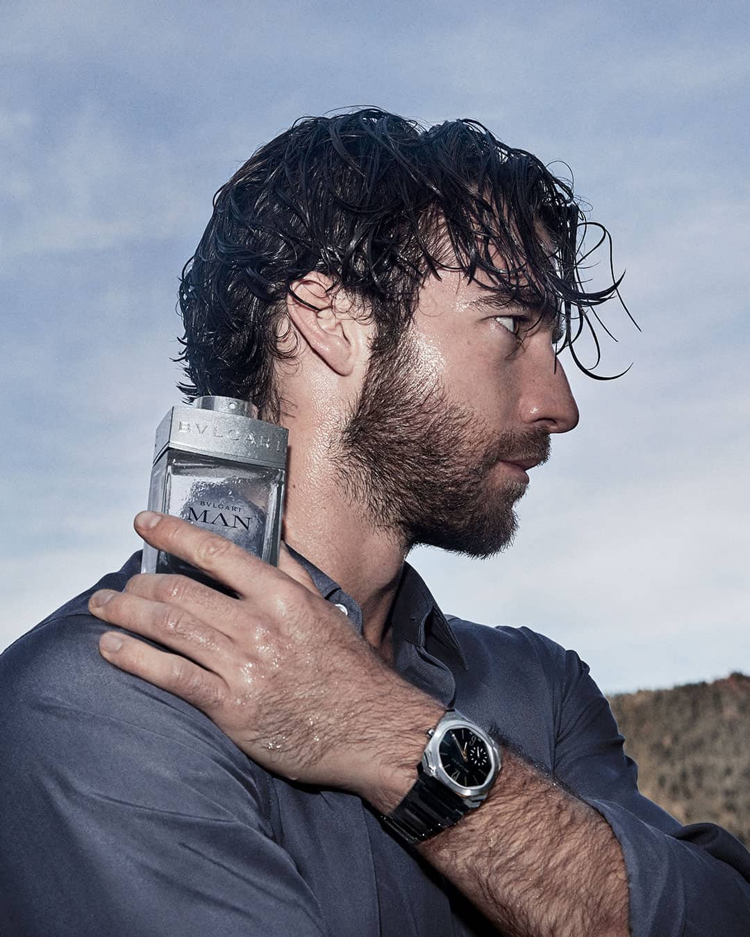 putting a bottle of bvlgari cologne to his shoulder