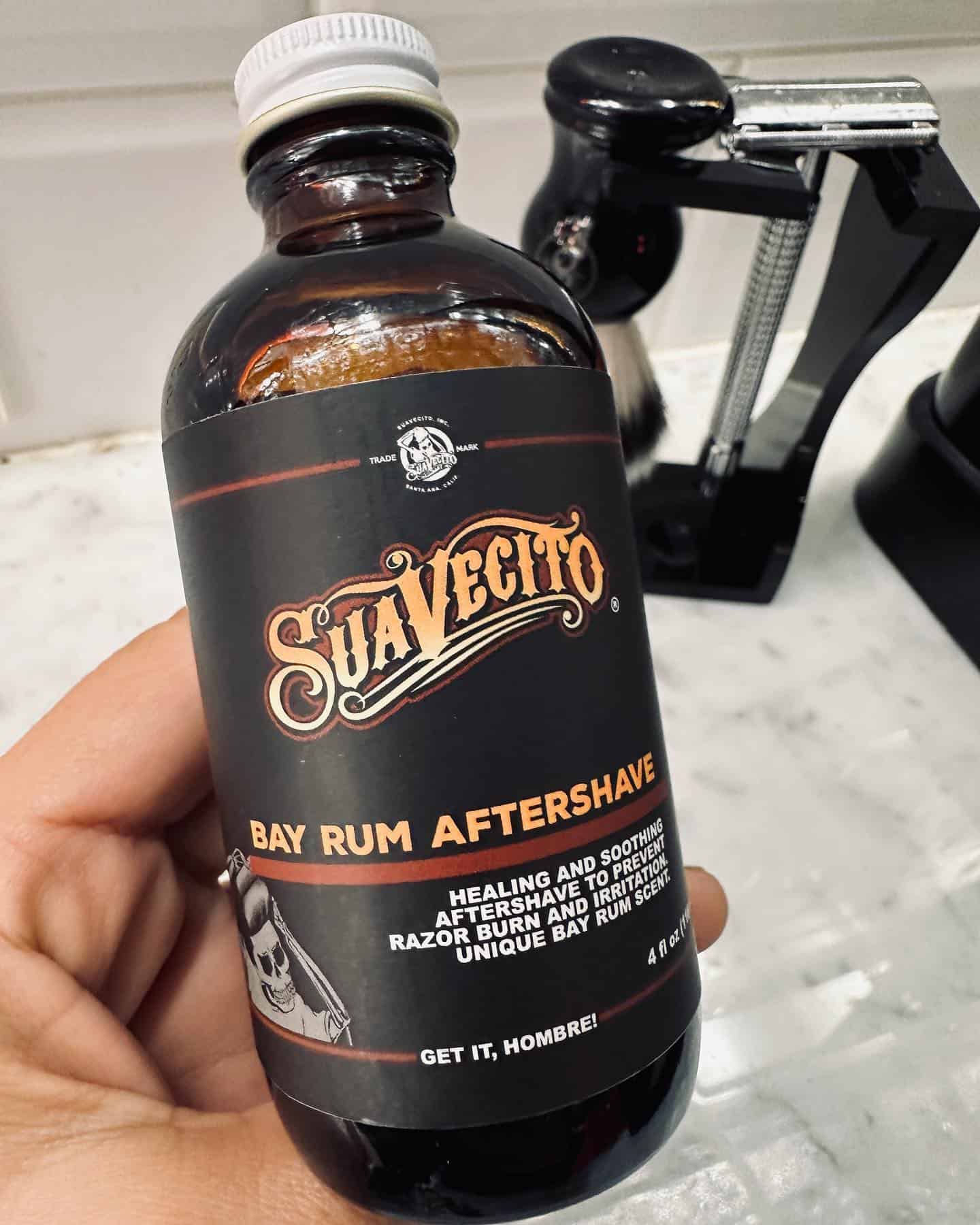 holding a bottle of suavecito bay rum after-shave