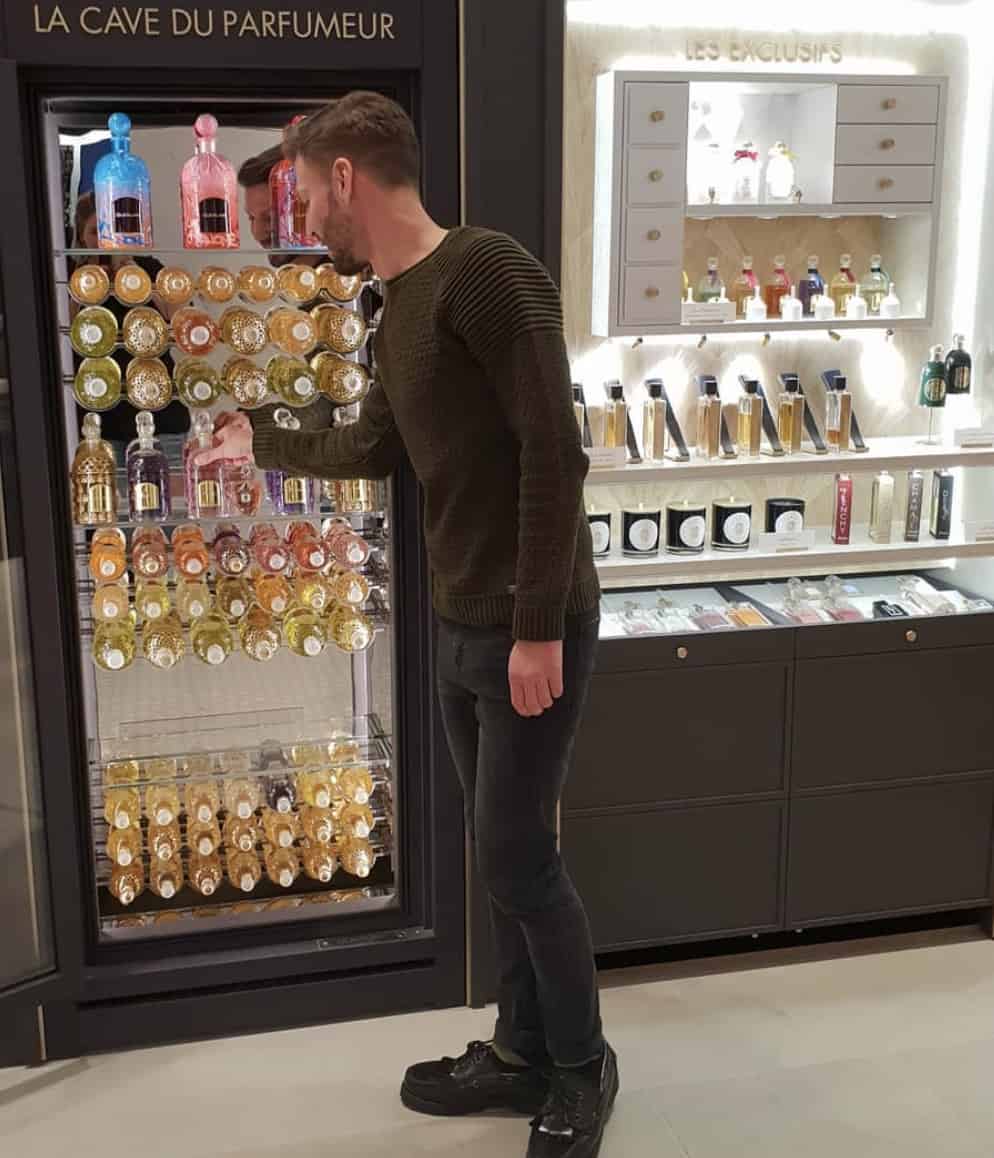 man pulling a bottle of perfume out of a large perfume fridge display