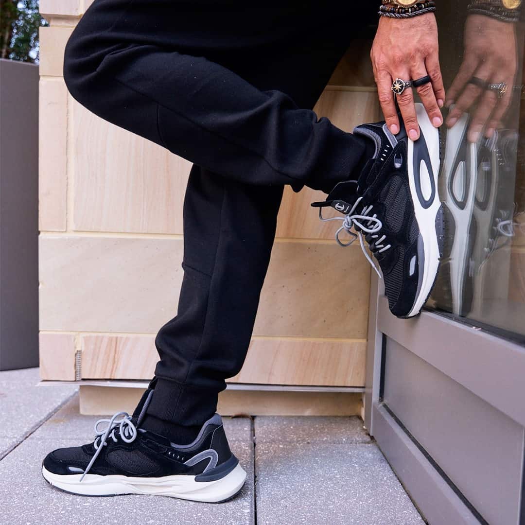 man standing on one leg leaning his back on a glass wall