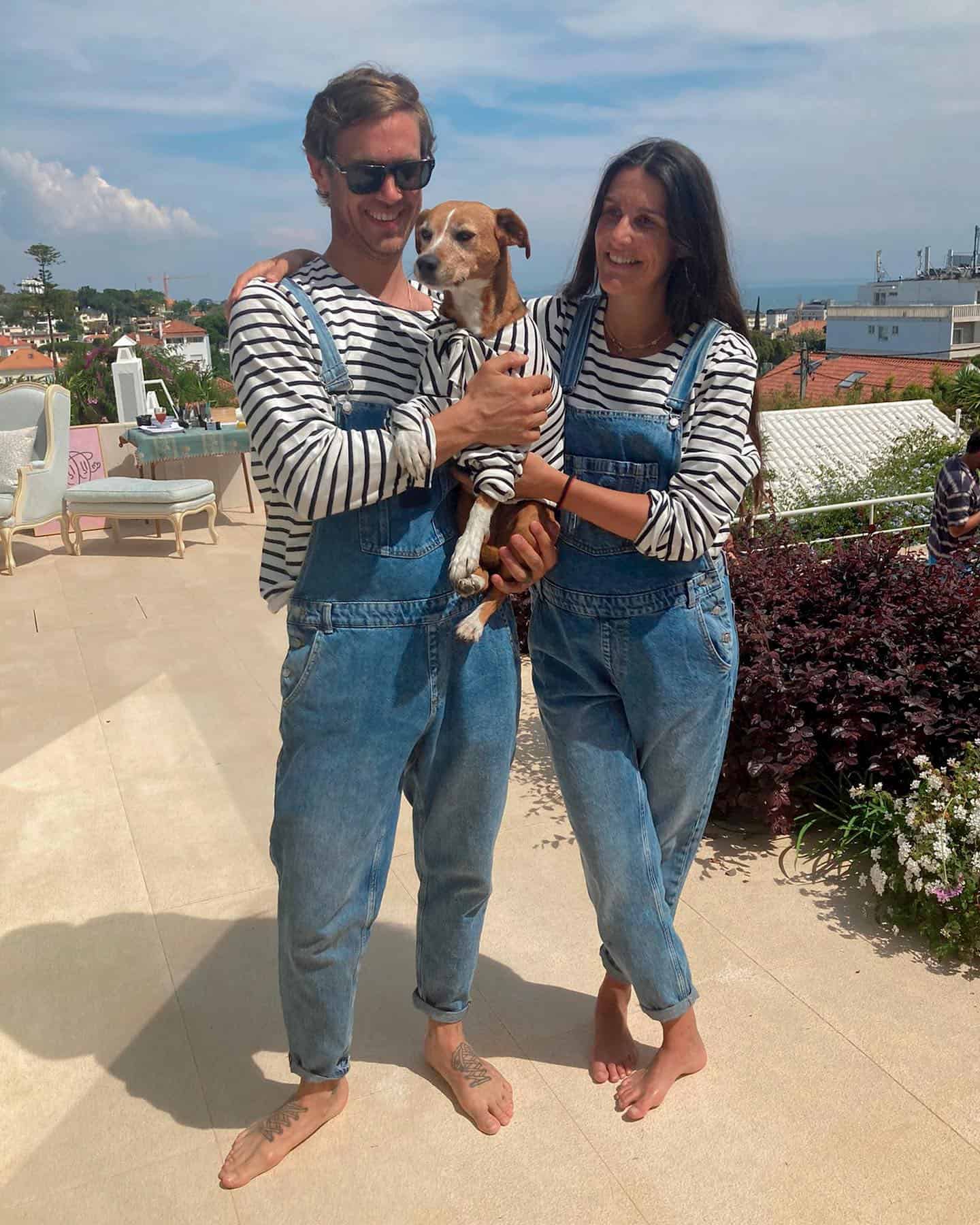Two people wearing overalls and striped long sleeve t-shirts holding a dog