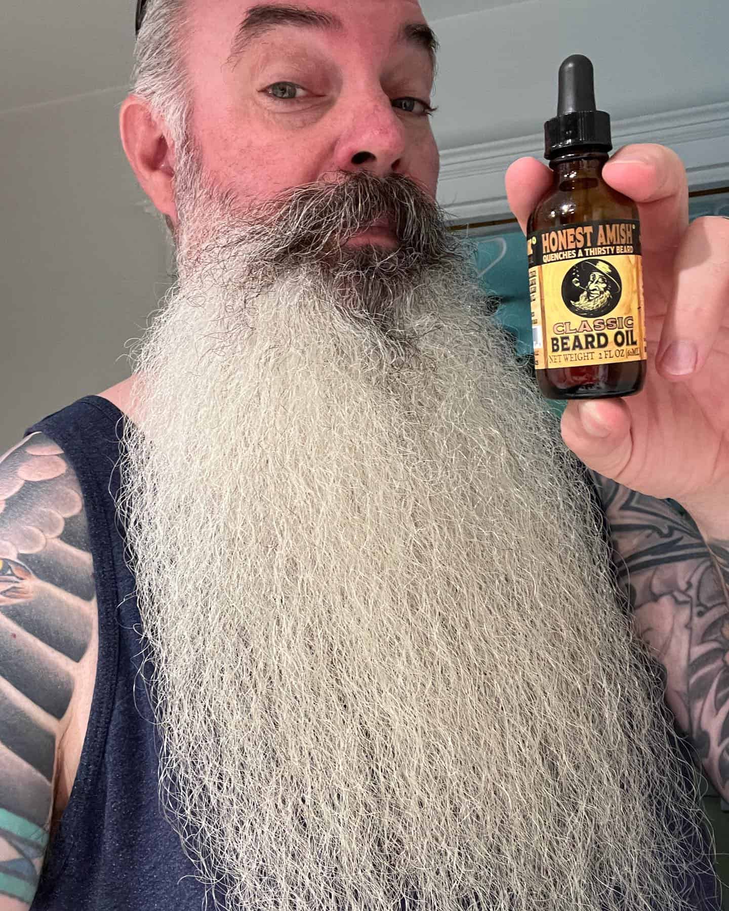 man with long white beard holding a bottle of classic beard oil by honest amish