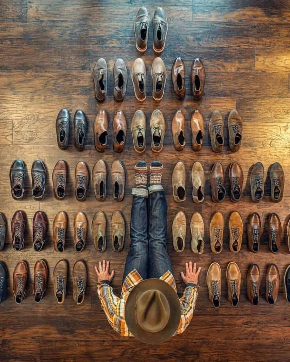 birds eye view of man sitting on the floor with a collection of leather boots