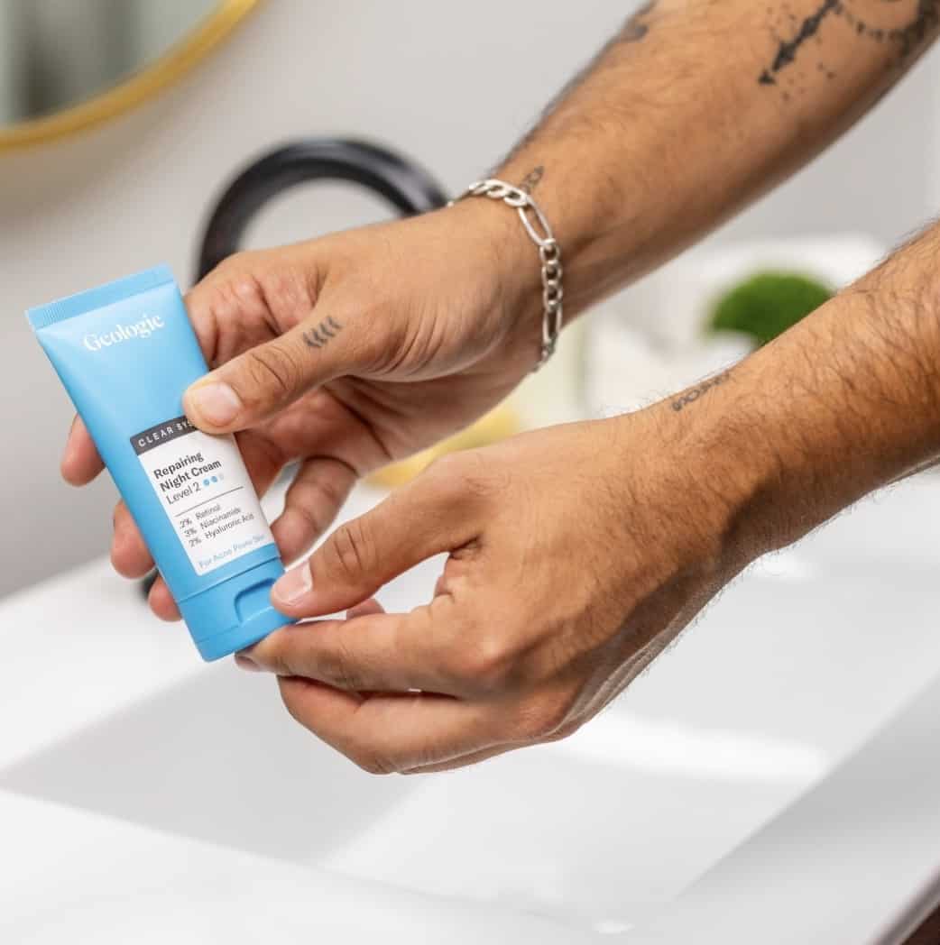 Male hands holding Geologie night cream over a bathroom sink