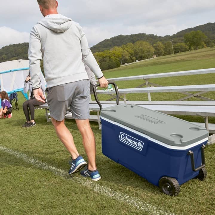 man pulling a wheeled cooler by coleman