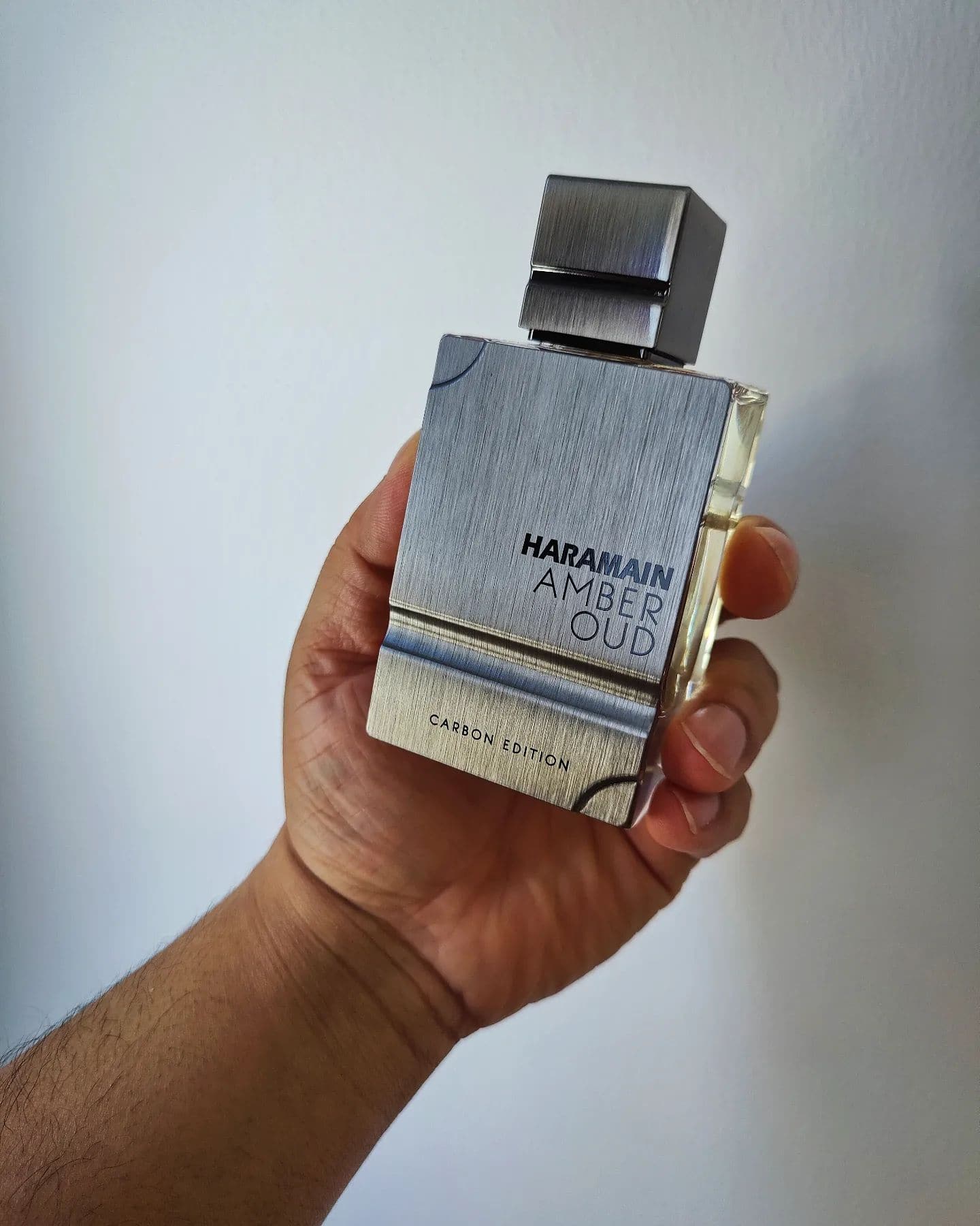 holding a bottle of al harmain amber oud carbon edition