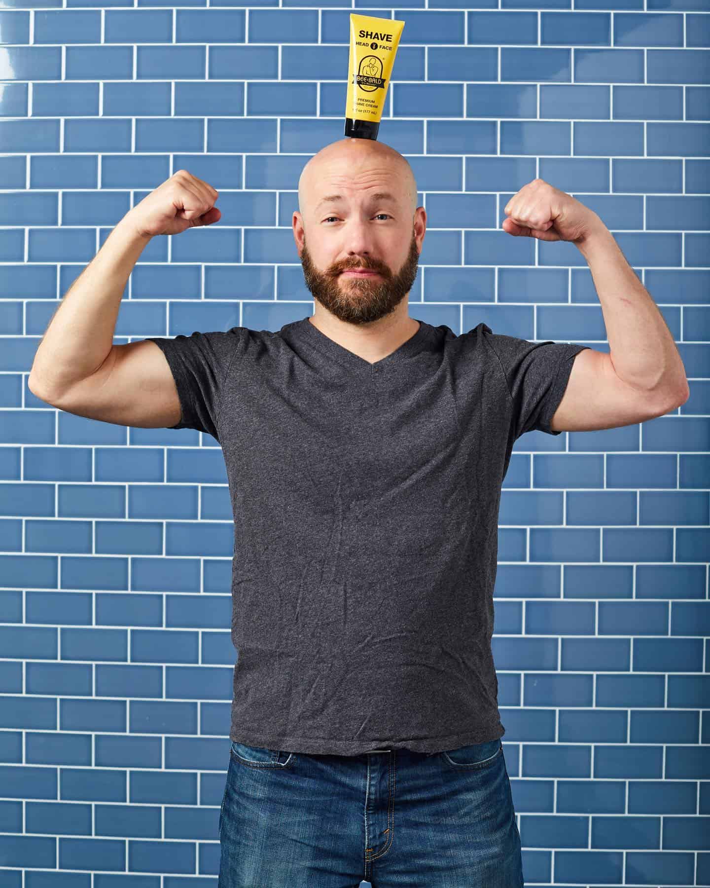 man flexing biceps and balancing a bee bald product on his head