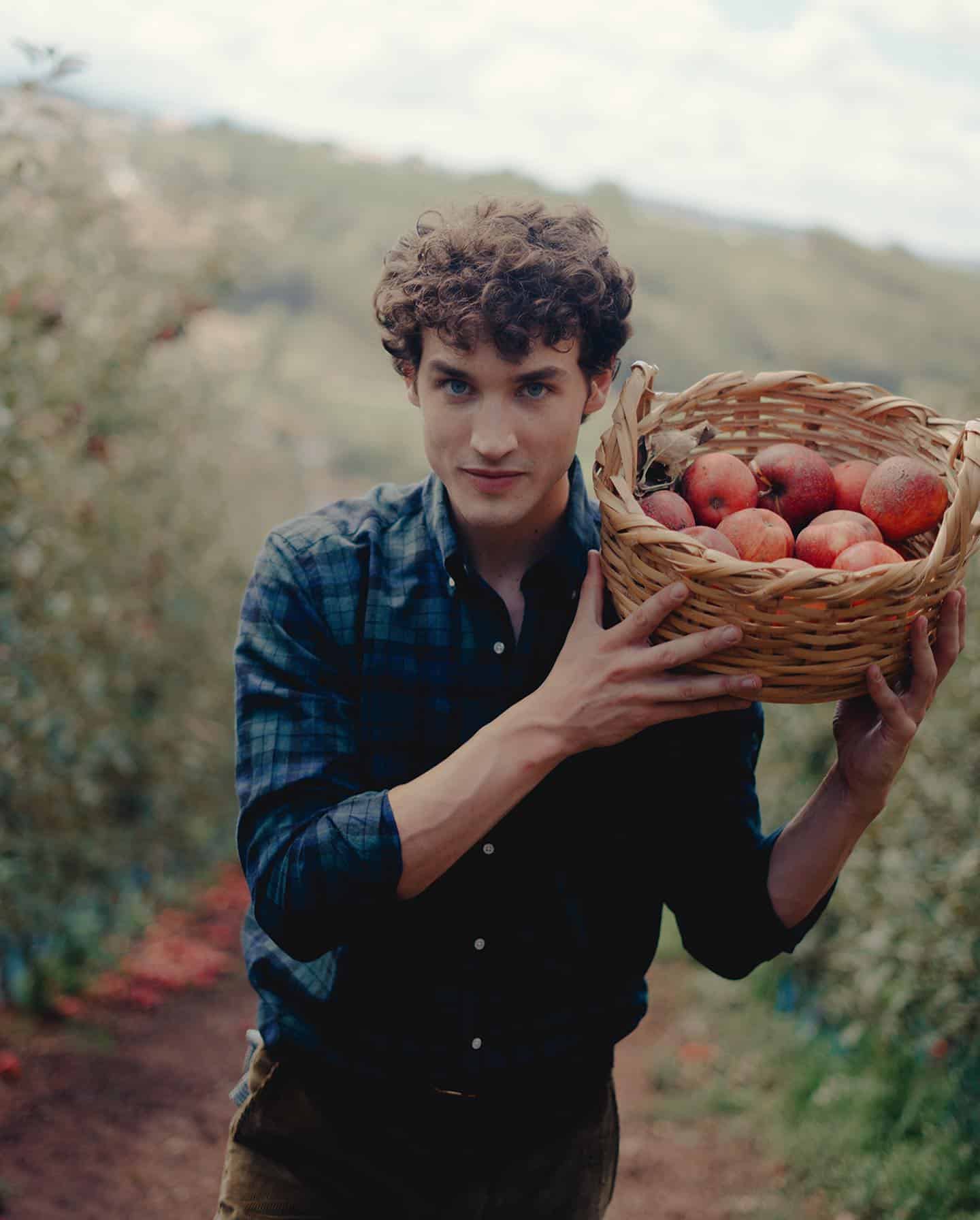 man carrying a basket of apples on his shoulder