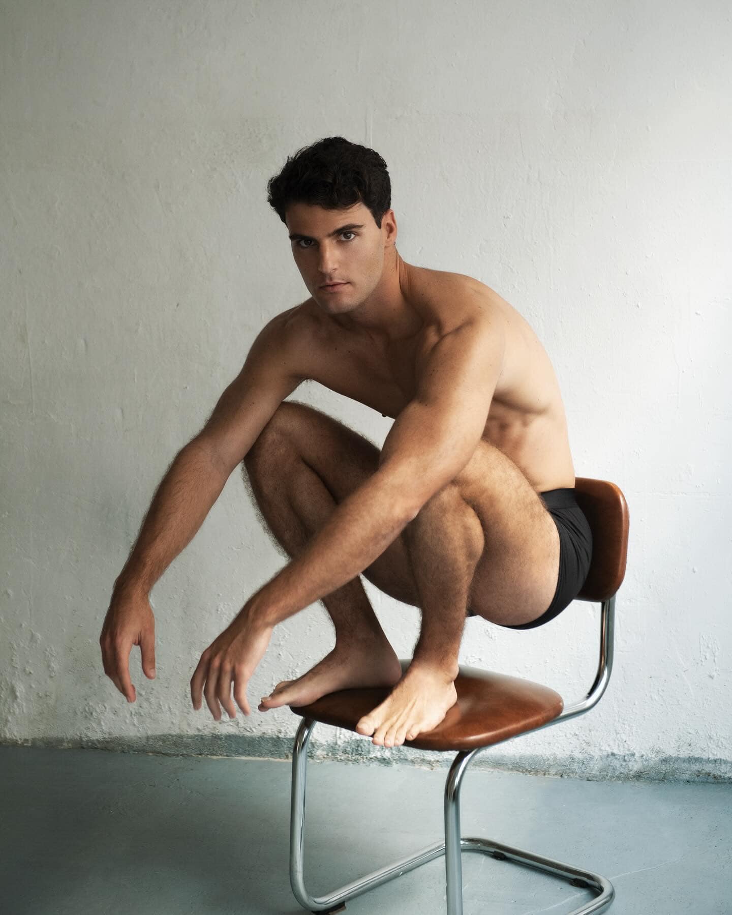 man in underwear squatting on top of a chair