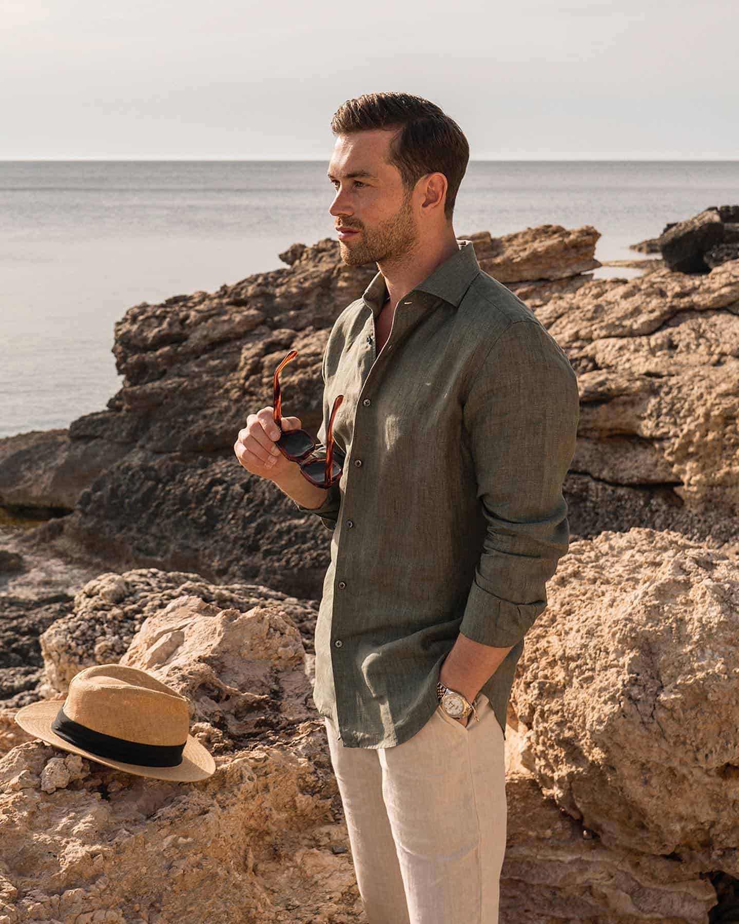 man holding his sunglasses while looking at the sea