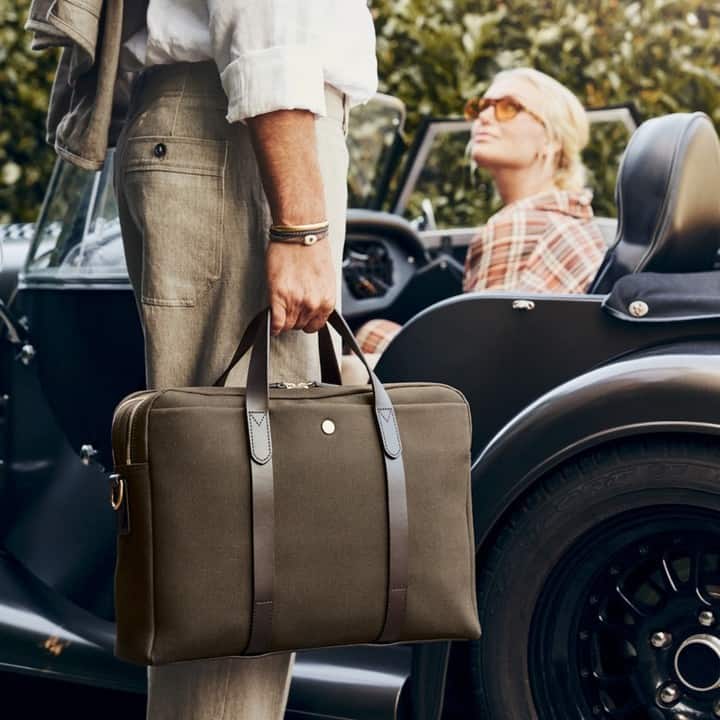 man carrying a laptop bag beside a classic car