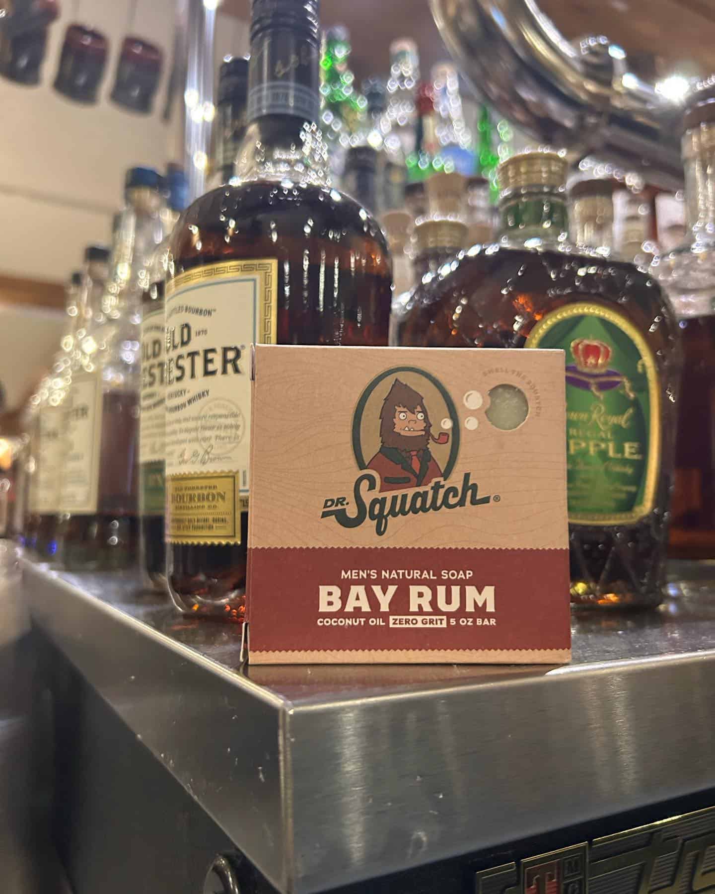 a bar of dr squatch bay rum soap in-front of bottles of liquors