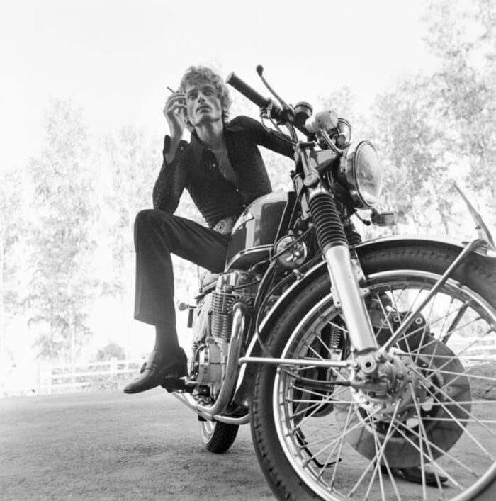 Man in 1970s smoking a cigarette on a parked motorcycle