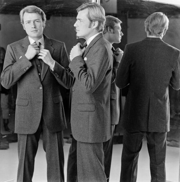 A man in 1980s checking his tie in a mirror