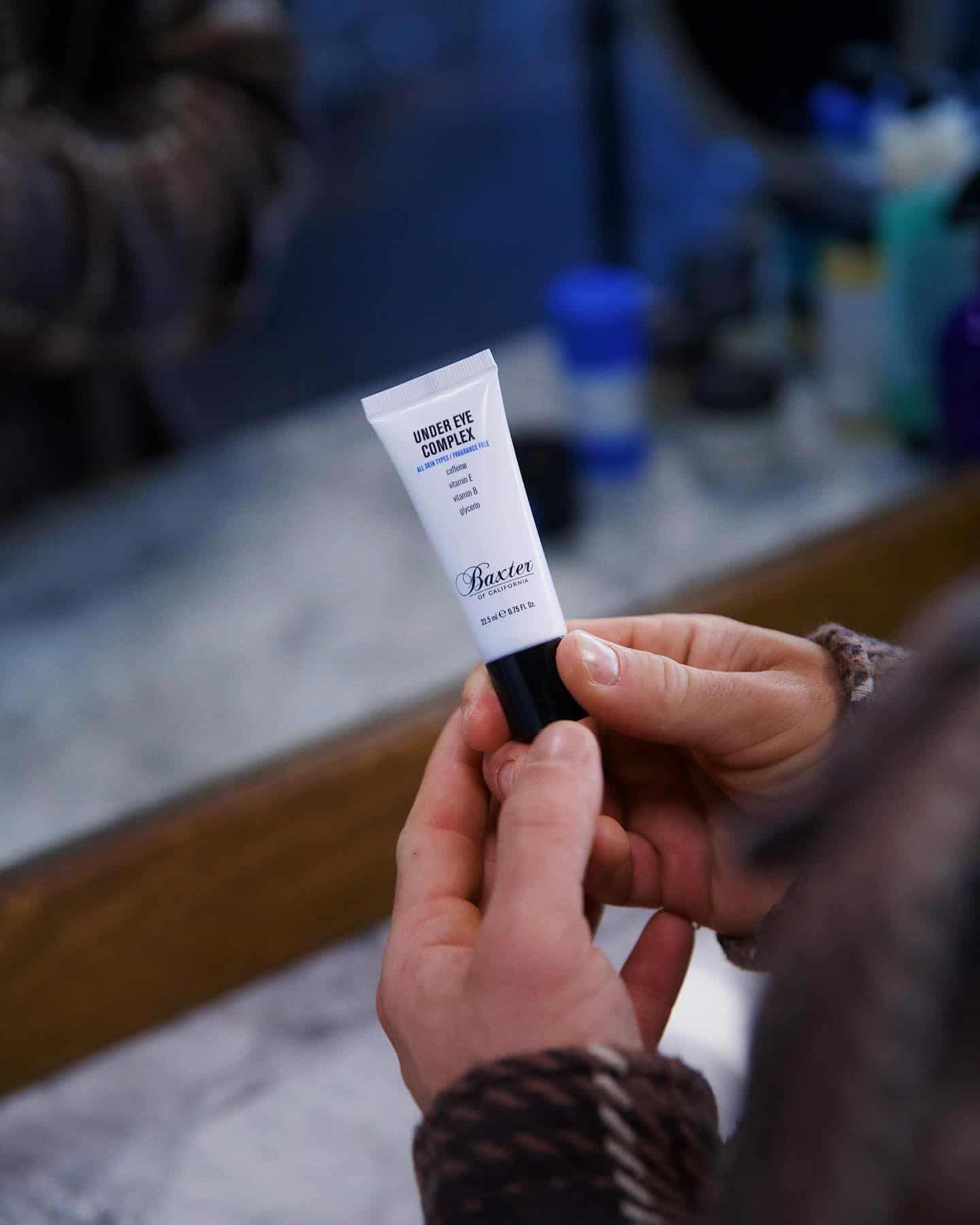 holding a tube of under eye complex by baxter of california