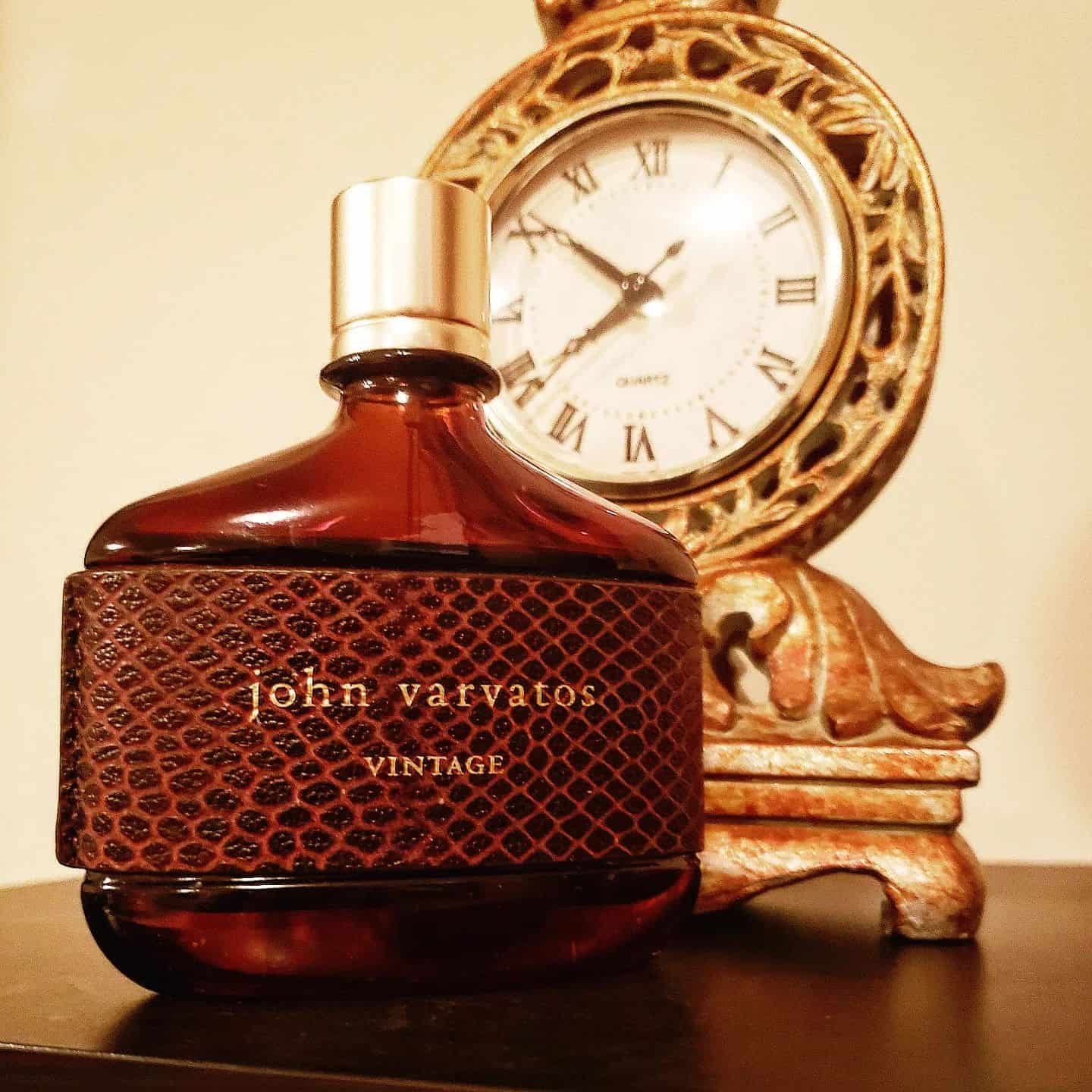 a bottle of john varvatos vintage cologne in-front of a desk clock