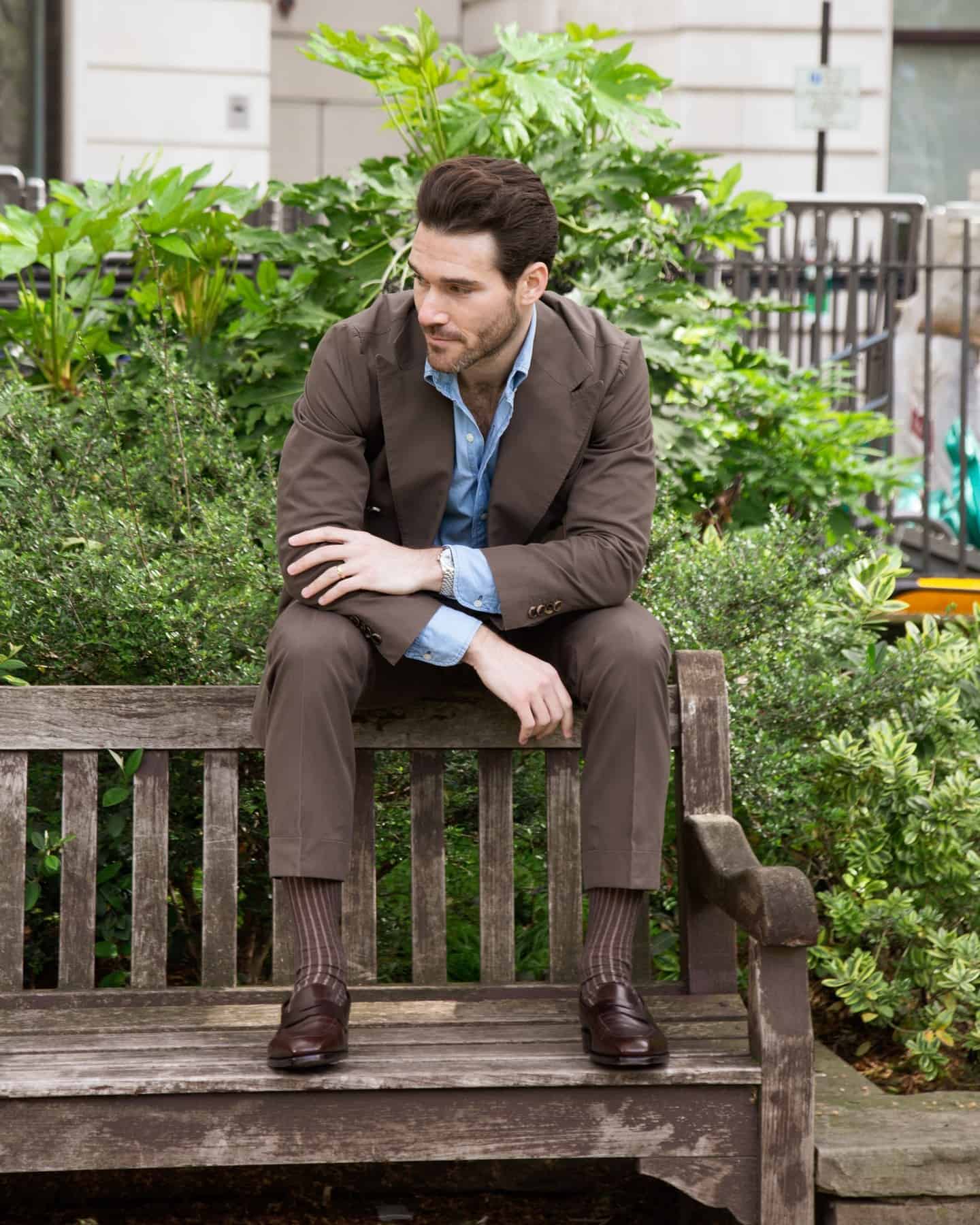 man in a brown suit sitting on top of a wooden bench