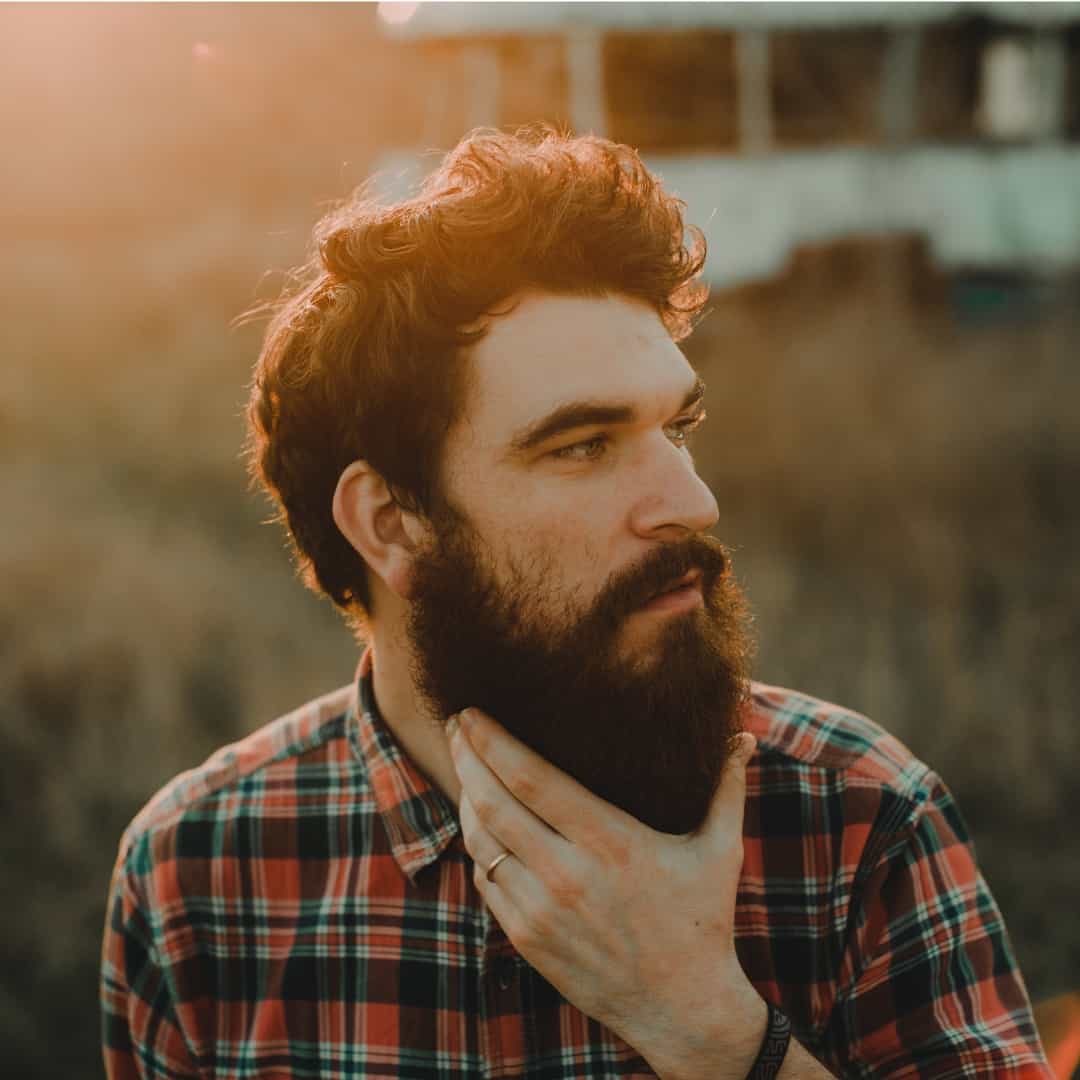 man in a checked shirt holding his beard