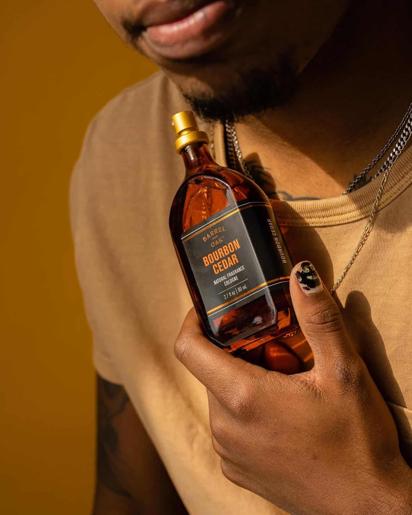 holding a bottle of barrel and oak natural fragrance cologne close to the chest
