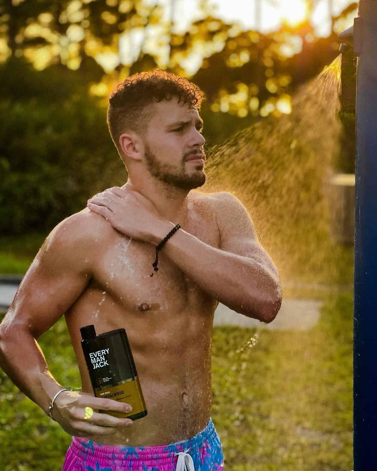 man taking a shower outdoors while holding a bottle of every man jack body wash