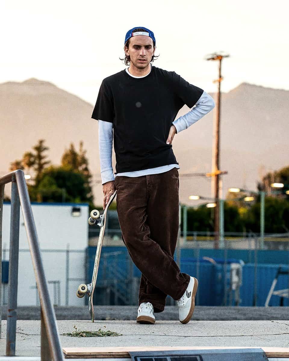 man standing cross legged and leaning on a skateboard