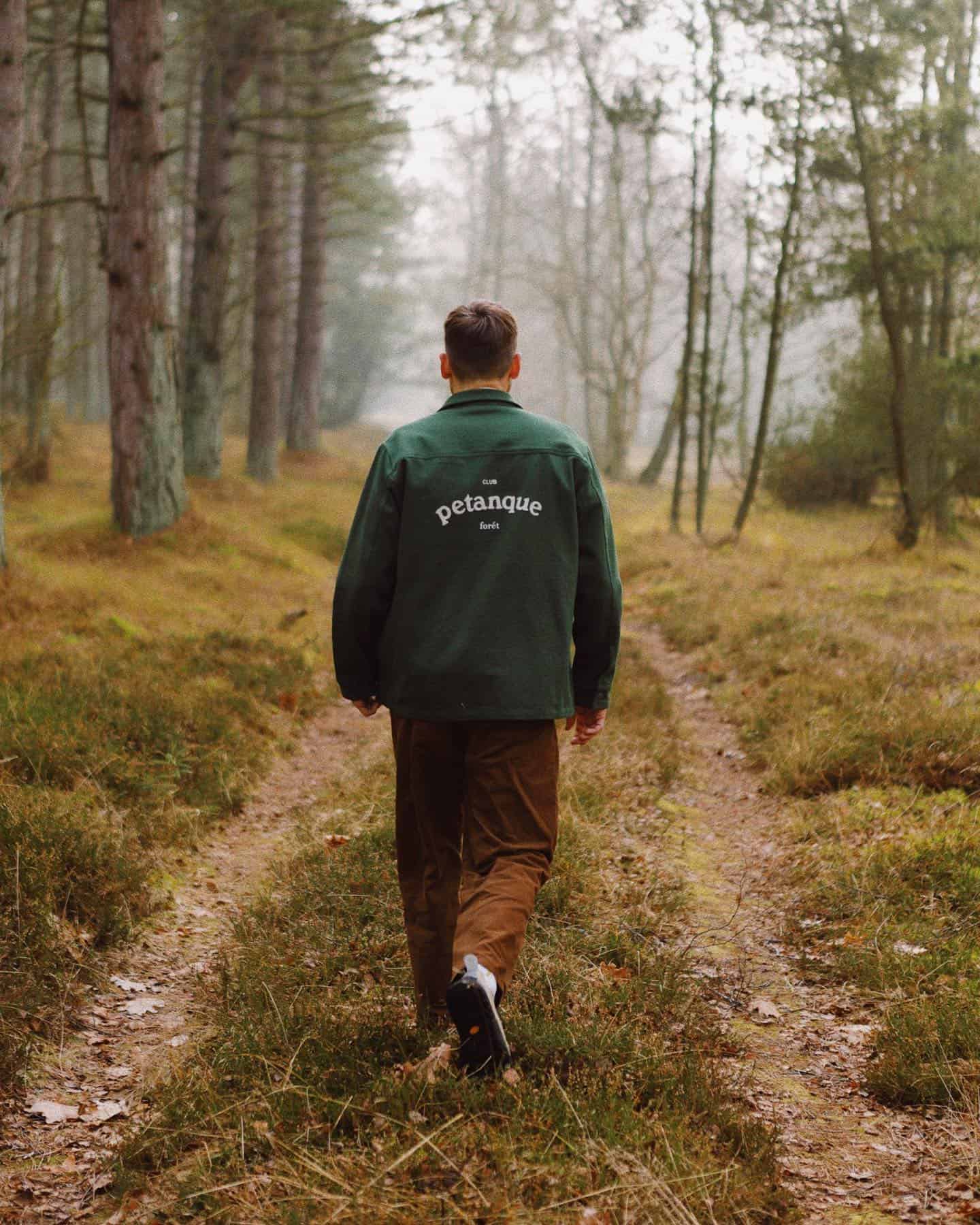 man in a green jacket walking the road to the woods
