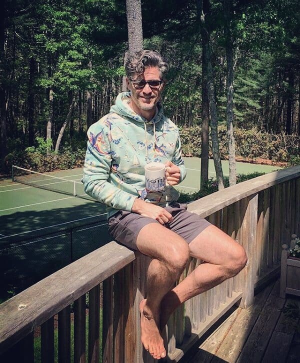 man sitting on a wooden fence while holding a cup of coffee