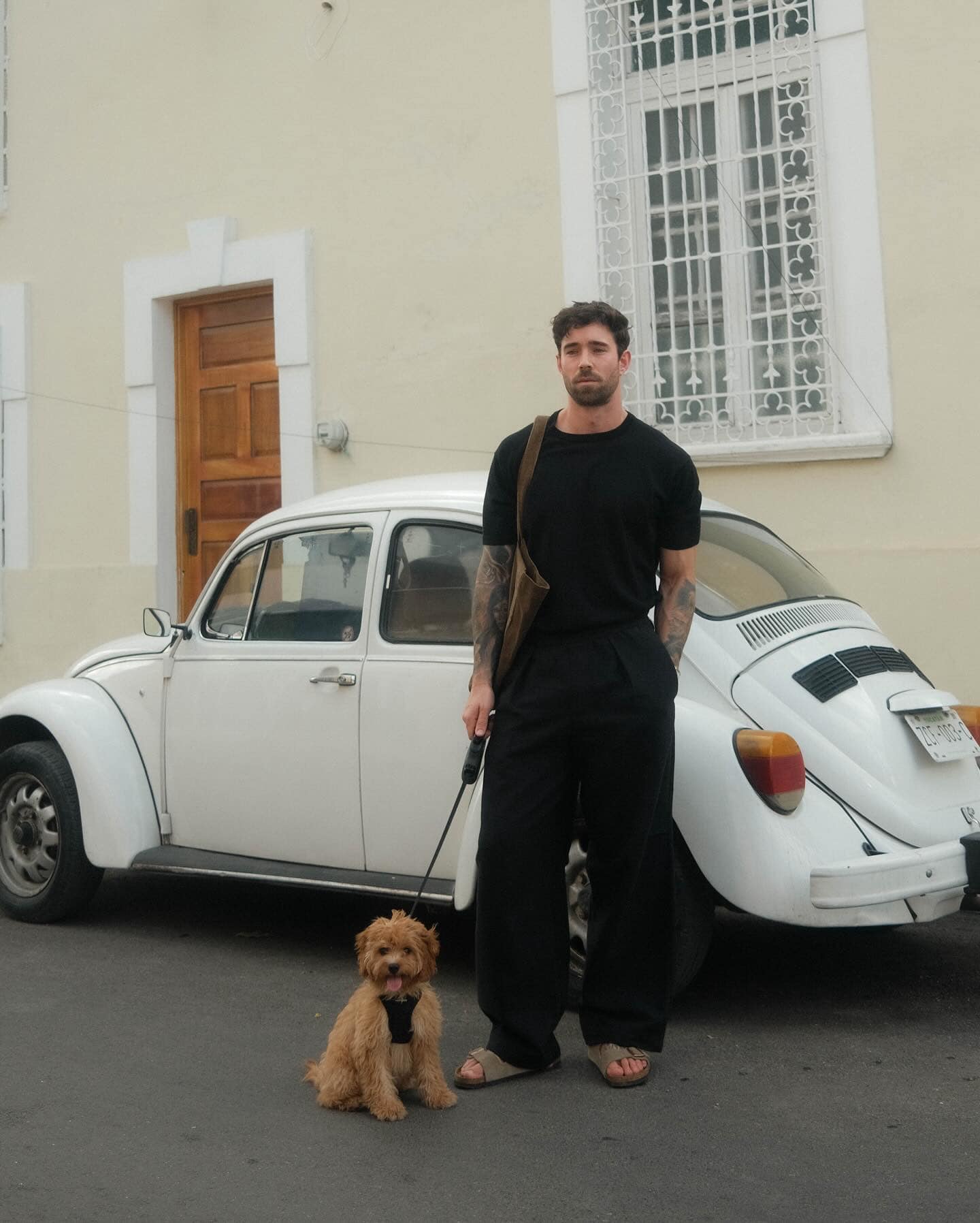 man in a black t-shirt and pants holding a dog on a leash