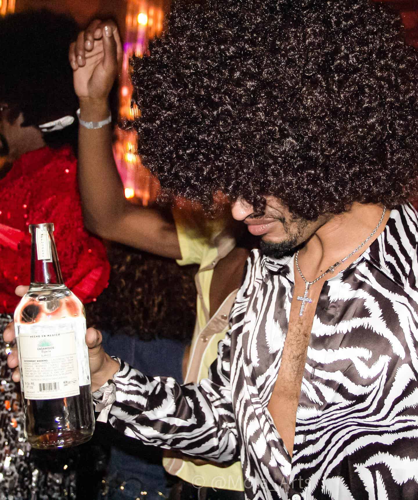 man with afro hair dancing while holding an empty bottle of tequila