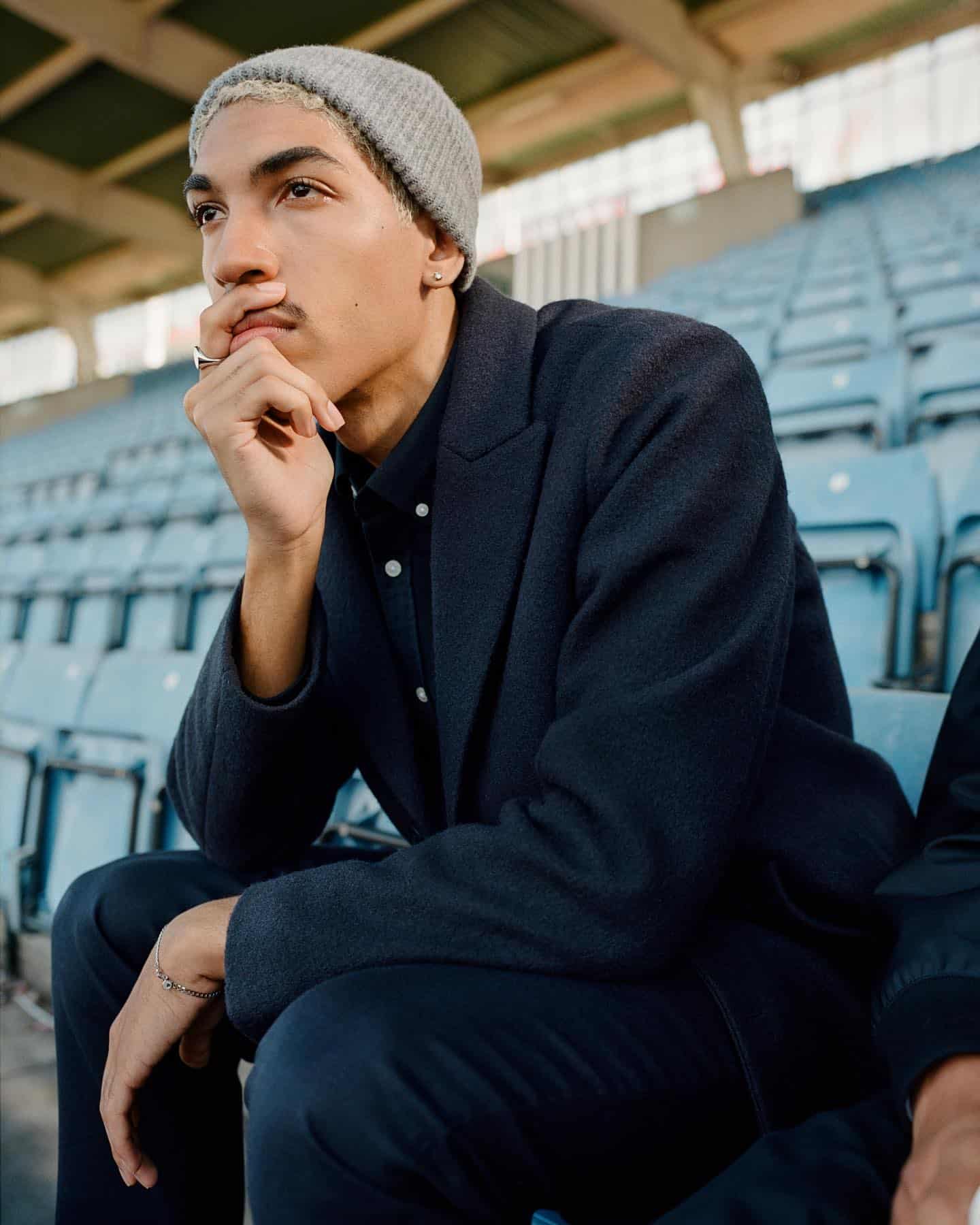Old Money style: man sitting on the bleachers wearing a wool coat and beanie