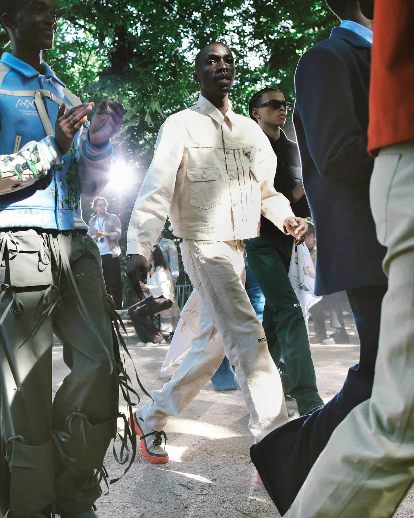 man in a fashion show wearing a white denim jacket and white jeans
