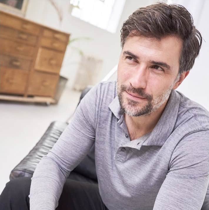 man sitting on a sofa wearing a long sleeved polo shirt
