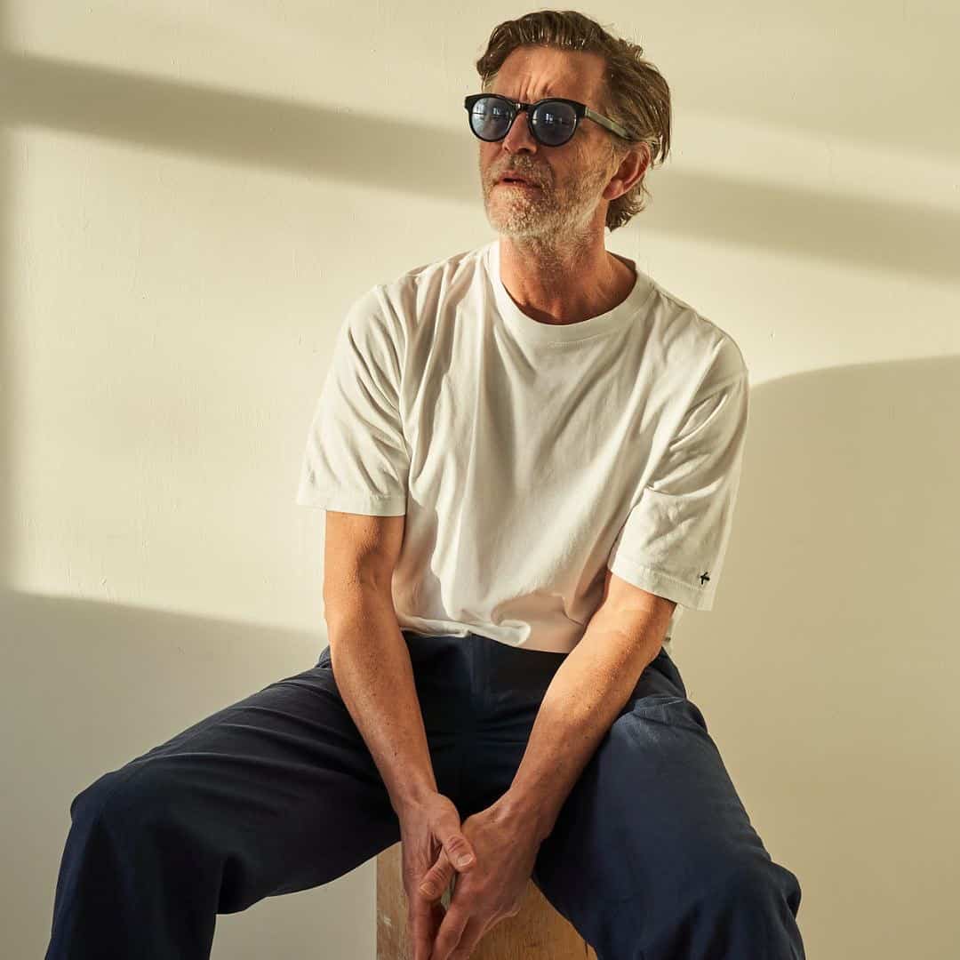 Normcore aesthetic: man sitting on a stool wearing white shirt and grey trousers
