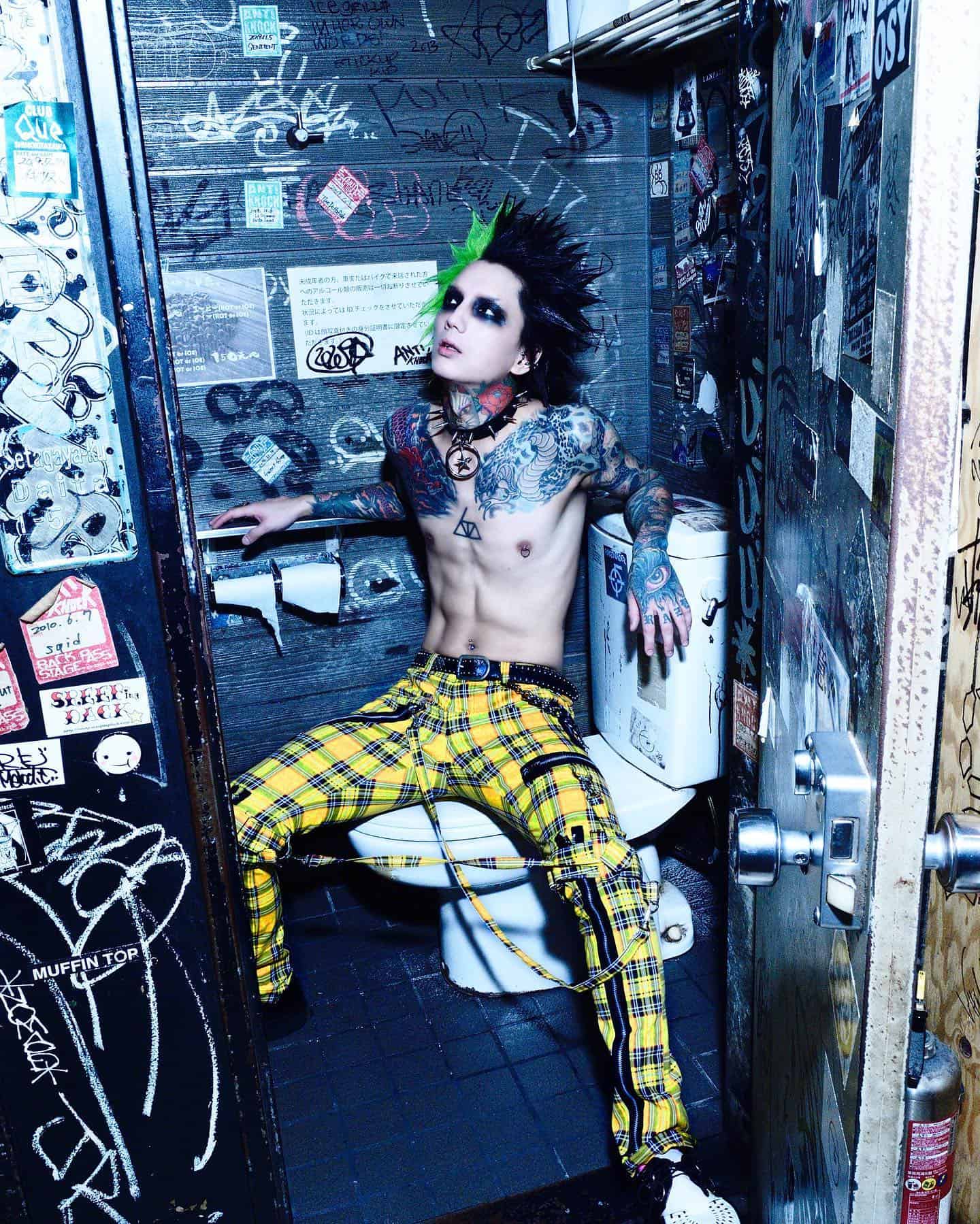 man wearing a yellow checked pants sitting on a toilet