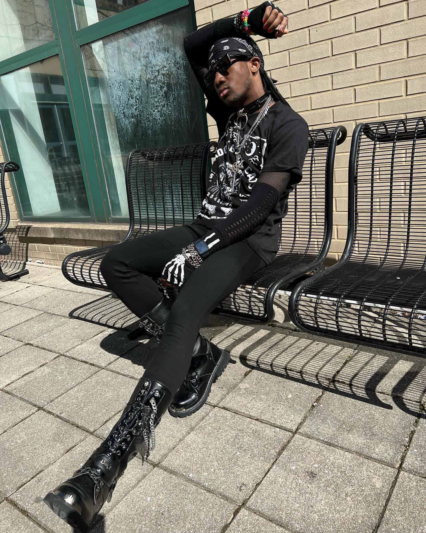 man in an all black outfit sitting on a metal bench