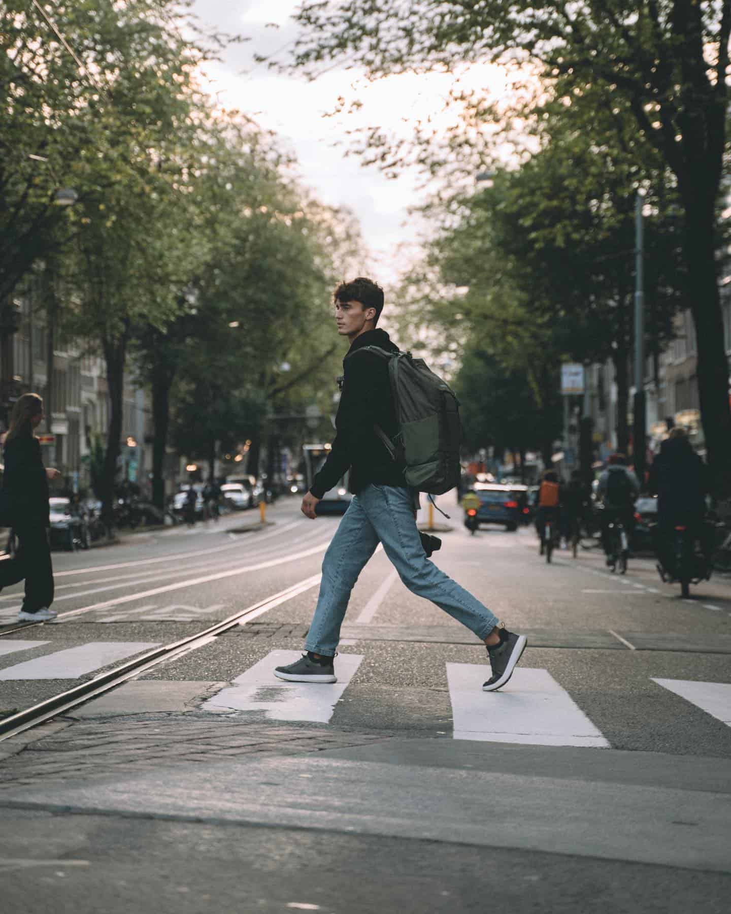 man wearing a jacket with backpack is crossing the street