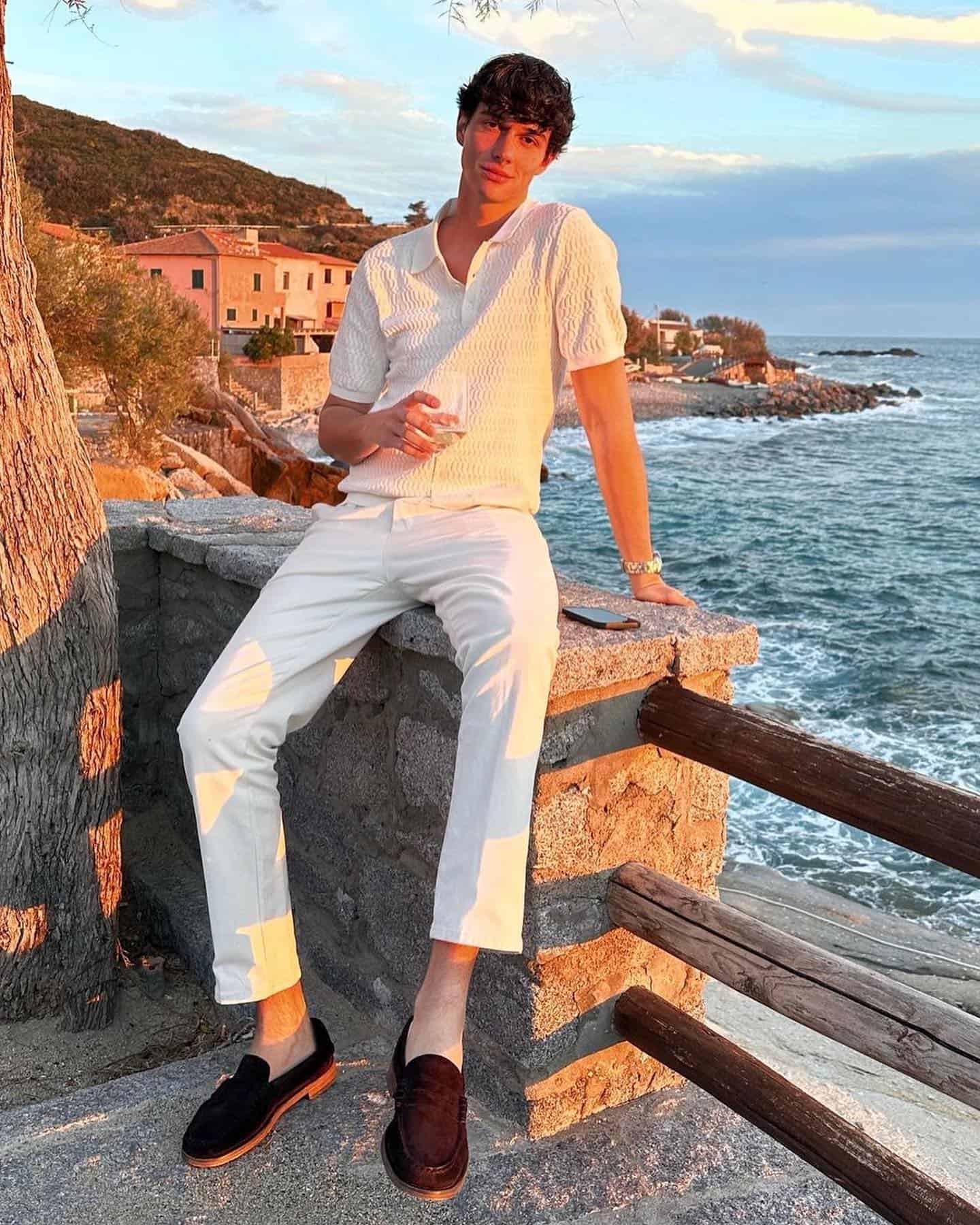 man sitting on a concrete fence wearing a white polo shirt and pants