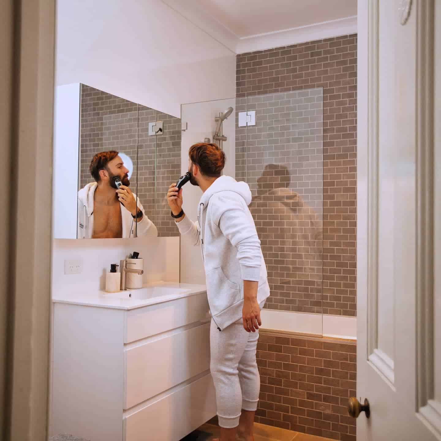 man shaving his beard infront of a mirror