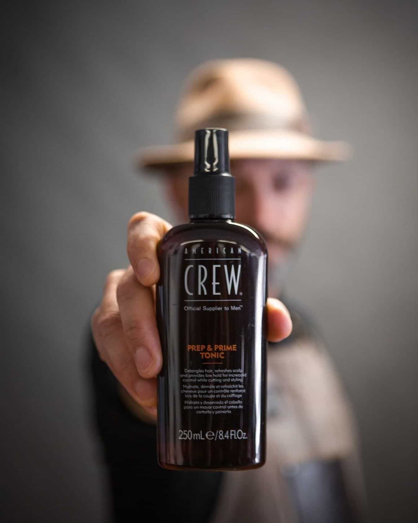man holding a bottle of american crew prep and prime tonic