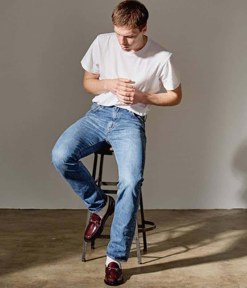 man sitting on a stool wearing a white t-shirt and jeans