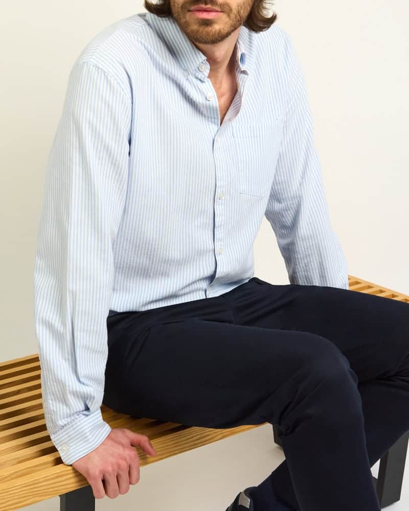 man sitting on a bench wearing a striped shirt and black pants