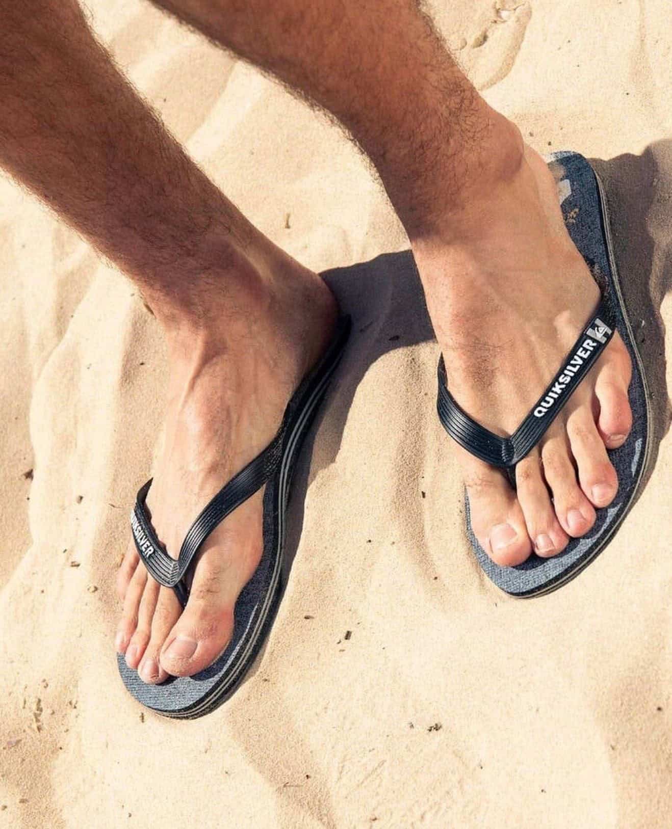 man standing on the sand wearing a pair of quicksilver flip flops