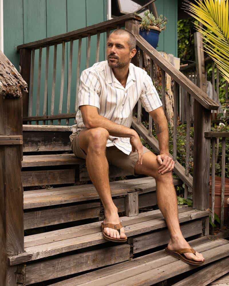 man sitting on a wooden stairs wearing short sleeved shirt and shorts