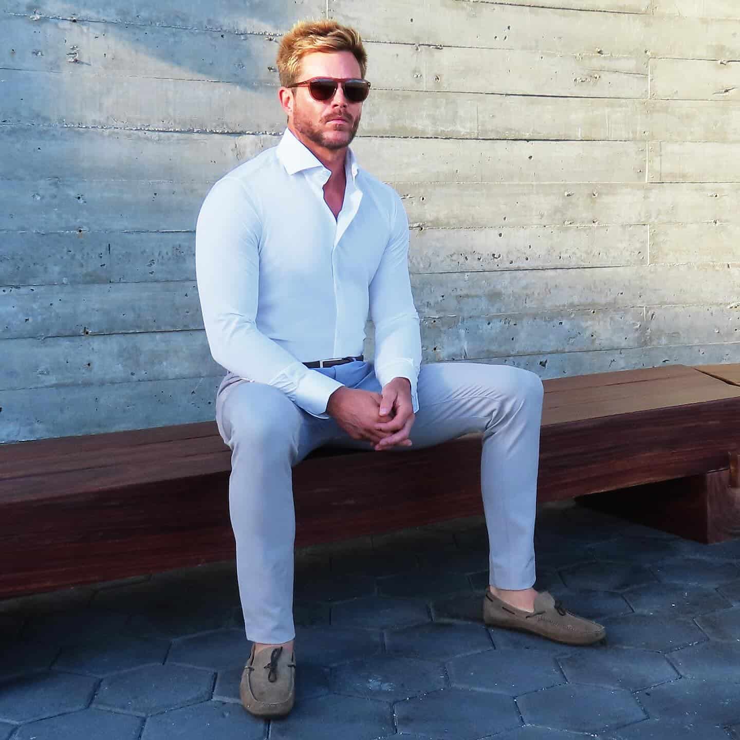 man sitting on a bench wearing a white shirt and grey pants